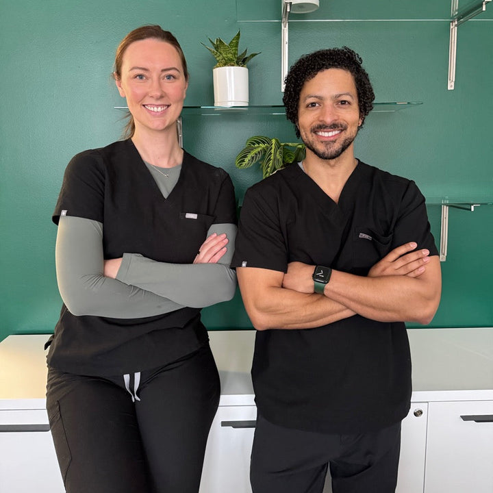 Two individuals in black scrubs standing in a room with green walls and shelves.